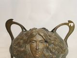 sculpture en bronze représentant le visage d'une femme, sur une plaque en laiton