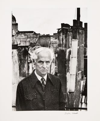 photographie en noir et blanc d'un homme en costume debout devant un immeuble
