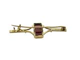 a close up of a gold plated brooch with a red stone