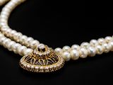 a close up of a necklace with pearls on a black background