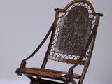 une vieille chaise en bois dont le dossier et l'assise sont sculptés, posée sur une surface blanche