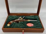 une boîte en bois contenant un pistolet et un pompon rouge