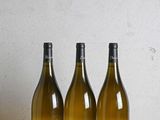 trois bouteilles de vin posées sur une table en bois, à côté d'une bouteille de vin