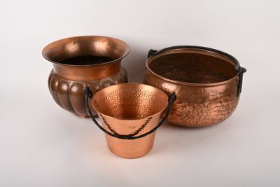 trois casseroles en cuivre posées les unes à côté des autres sur une surface blanche