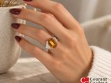 woman ' s hand holding a yellow sapphire and diamond ring in front of a vase of flowers