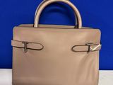 un sac à main beige posé sur une table blanche, sur fond bleu