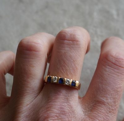 la main d'une personne portant une bague en or sertie de pierres bleues et blanches