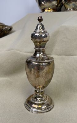 une urne en argent posée sur une table, avec d'autres objets en argent en arrière-plan