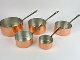 six copper pots and spoons are lined up on a white surface