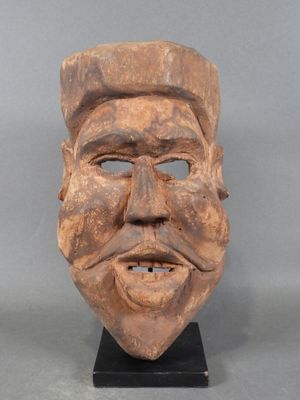 un gros plan d'un masque en bois représentant un visage, posé sur un socle