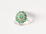 a close up of a ring with green stones on a white surface