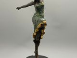 une statue représentant une femme en robe verte, posée sur un socle noir