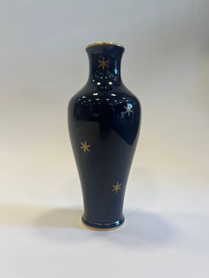 blue vase with gold stars on it sitting on a white surface