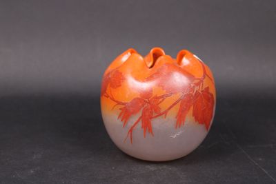 orange and white vase with leaves on it sitting on a black surface
