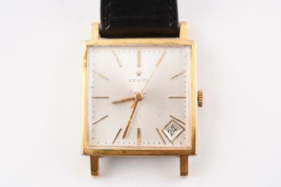 une montre en or avec un bracelet en cuir noir posée sur un fond blanc