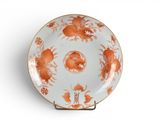 une assiette orange et blanche posée sur un support, sur une surface blanche
