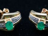 une paire de boucles d'oreilles en émeraude et diamant posées sur un fond noir