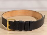 ceinture en cuir noir avec boucle dorée posée sur une surface en bois