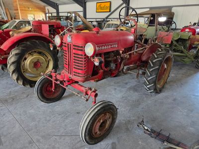 a red tractor parked in a garage next to other tractors