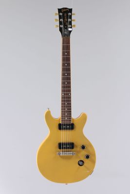 une guitare électrique jaune accrochée à un mur blanc