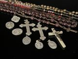 plusieurs chapelets et une croix posés sur une table, sur fond noir