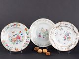trois assiettes ornées de fleurs et de noix, posées sur un fond noir
