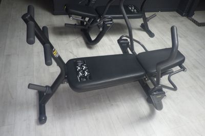 un banc noir posé à même le sol, à côté de deux appareils de musculation