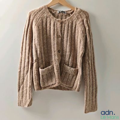 a brown sweater hanging on a hanger against a wall