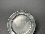 an old silver plate on a black surface with a small hole in the middle