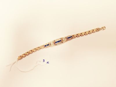 a gold bracelet with blue stones on it on a white surface