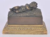 une statue en bronze représentant un bébé allongé sur un lit
