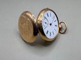 une montre de poche en or avec un cadran blanc sur une surface blanche