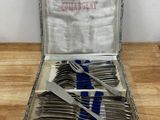 des couverts dans un coffret en argent posé sur une table en bois ornée d'un ruban bleu