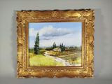 une peinture à l'huile représentant une route de campagne, dans un cadre doré accroché au mur
