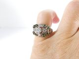 a woman ' s hand holding a diamond and emerald ring