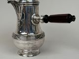 an antique silver coffee pot with a wooden handle on a white surface