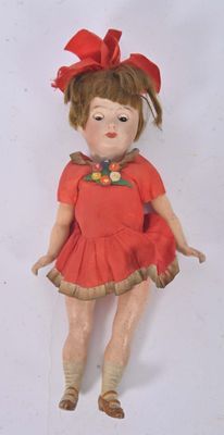 une petite poupée avec une robe rouge et un nœud rouge