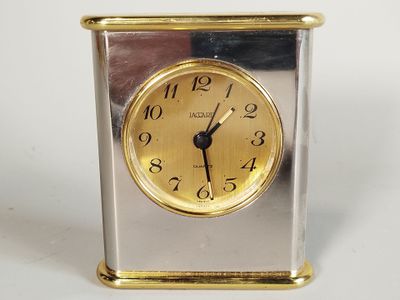 une horloge argentée et dorée posée sur une surface blanche
