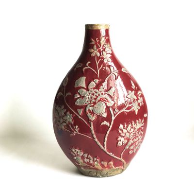 un vase rouge orné de fleurs blanches, posé sur un fond blanc