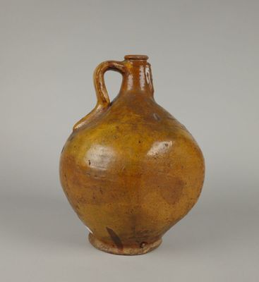 un vieux vase marron muni d'une anse, posé sur une surface blanche