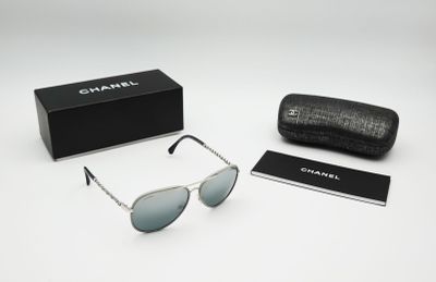 Des lunettes de soleil Chanel et leur étui posés sur une surface blanche, avec une boîte noire