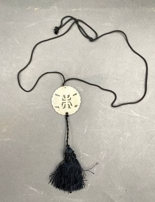 un pompon noir orné d'un disque blanc sur lequel figure une inscription en chinois