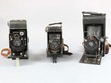 three old cameras sitting side by side on a white surface
