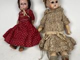two old dolls sitting next to each other on a white surface