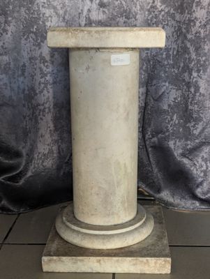 un socle en marbre blanc à base ronde posé sur un sol carrelé