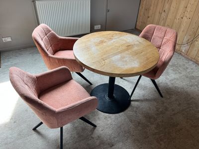 pink chairs and a round table in a room with a radiator