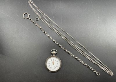 une photo représentant une montre de poche en argent avec sa chaîne, posée sur une table