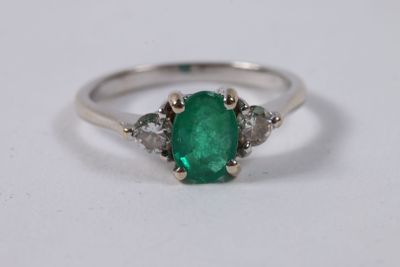 a close up of an emerald and diamond ring on a white surface