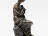 a bronze statue of a woman sitting on a rock