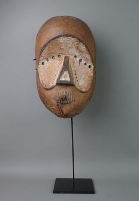 une image représentant un masque en bois posé sur un socle, sur fond gris